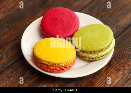 Tre tradizionali francesi macaron colorati sulla piastra di sfondo di legno Foto Stock