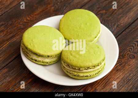 Tre francese tradizionale pistacchio macarons sulla piastra, scuro dello sfondo in legno Foto Stock