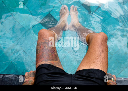 Mans gamba con tatuaggi sul lato di una piscina. Foto Stock