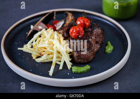 Filetto di manzo con patatine fritte di stringa, arrosto di pomodori e funghi champignon Foto Stock