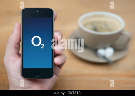Un uomo guarda al suo iPhone che consente di visualizzare l'O2 logo, mentre sat con una tazza di caffè (solo uso editoriale). Foto Stock