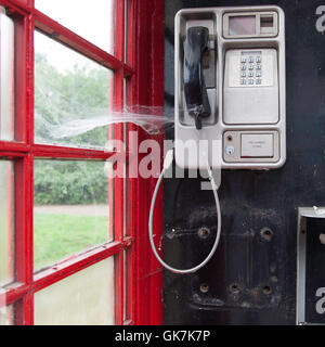 Una tradizionale scatola telefonica pubblica rossa in un ambiente rurale nel Regno Unito mostra il web di un ragno sul ricevitore. Simbolo di obsolescenza. Raramente usato telefono box con ciottwebs a Waveney, Inghilterra Foto Stock