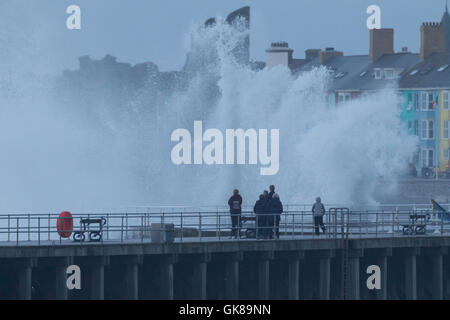 Persone in piedi su un pontile come grandi onde infrangersi contro la difesa del mare. Credito: Ian Jones/Alamy Live News Foto Stock