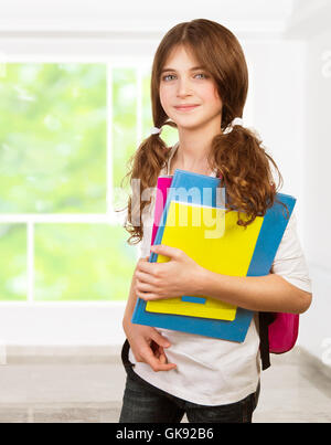 Bella ragazza in piedi in aula con libri di testo colorato in mani, studiando con piacere, si torna a scuola Foto Stock