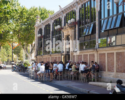 Le persone aventi il pranzo al di fuori di les halles il mercato alimentare di sale nel centro della città di Narbonne, Languedoc Roussillon, Francia Foto Stock