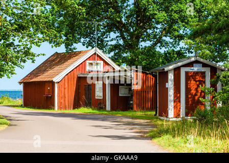 Ekenas, Svezia - 10 agosto 2016: piccoli e rossi capanne in legno lungo la strada del villaggio. Costa in background e albero canopy dando s Foto Stock