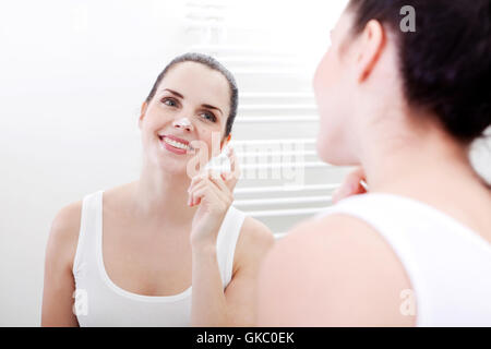 Bruna giovane donna ragazza con la crema nella stanza da bagno Foto Stock