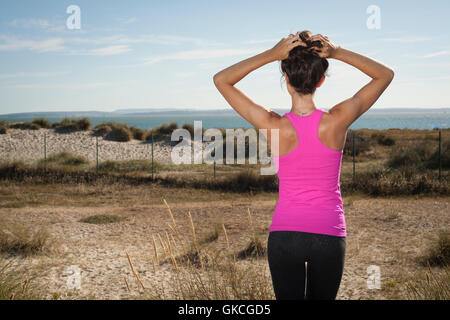 Guardando al mare regolando i suoi capelli dopo esercizio e di mantenersi in forma Foto Stock