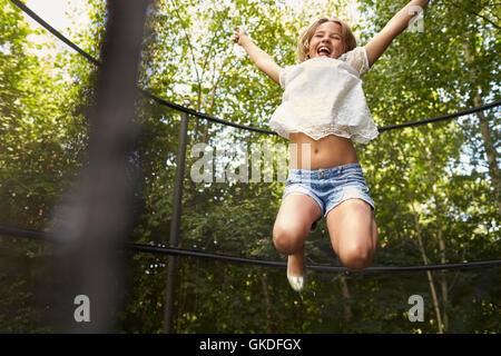 Ragazza divertirsi saltando sul trampolino in un giardino Foto Stock