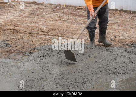 Lavoratore utilizzare hoe su un nuovo pavimento di calcestruzzo colato in sito in costruzione Foto Stock