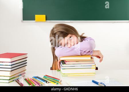 Schoolgirl appoggiata su una pila di libri Foto Stock