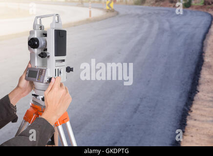 Lavorazione a mano con attrezzature di indagine teodolite su un treppiede. con la strada in costruzione sullo sfondo Foto Stock