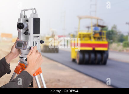 Lavorazione a mano con attrezzature di indagine teodolite su un treppiede. con la strada in costruzione sullo sfondo Foto Stock