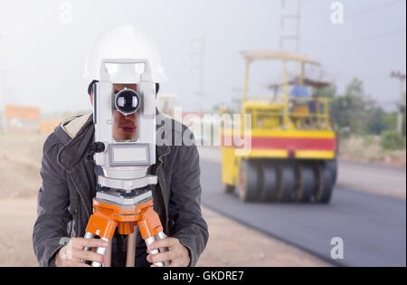 Ingegnere di lavoro con attrezzature di indagine teodolite con la strada in costruzione sullo sfondo Foto Stock