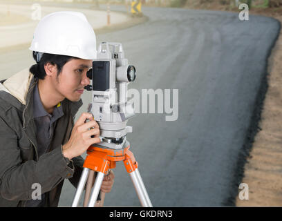 Ingegnere di lavoro con attrezzature di indagine teodolite con la strada in costruzione sullo sfondo Foto Stock