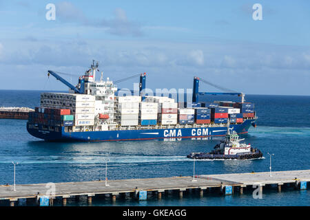 Un grande rimorchiatore lungo un enorme, caricato CMA CGM freighter in St Maarten Foto Stock