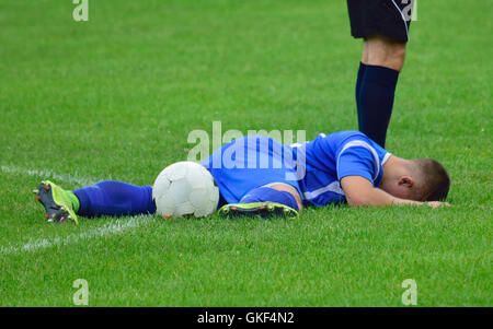 Giocatore di calcio feriti sdraiati sull'erba con una sfera Foto Stock