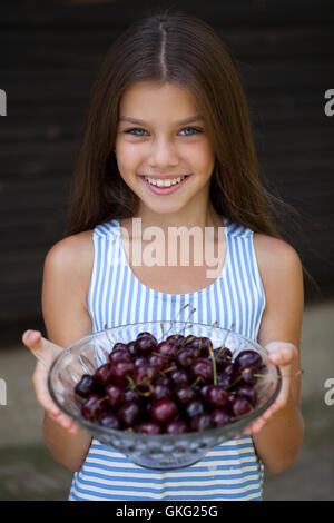 Bella bruna piccola ragazza con una ciotola di ciliegie in giardino Foto Stock