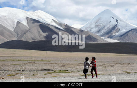 Golmud, Qinghai, Cina. 21 Ago, 2016. mostra due bambini tibetani giocando al di sotto del picco Yuzhu della parte orientale dei monti Kunlun nel nord-ovest della Cina di Provincia di Qinghai. Il 6,178-metro-alto picco Yuzhu è il più alto dei monti Kunlun nella vicina Qinghai, e che è considerato come il luogo migliore per arrampicata principianti come il suo percorso richiede meno tecnica. Credito: Zhang Hongxiang/Xinhua/Alamy Live News Foto Stock