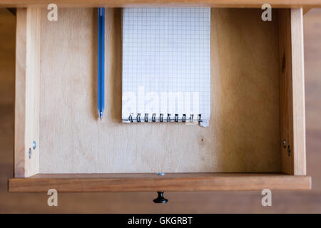 Vista al di sopra della moderna penna e taccuino a quadretti in aprire il cassetto del comodino Foto Stock