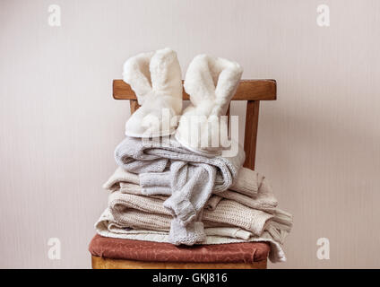 Pila di vestiti caldi sulla sedia, coppia di caldo inverno pantofole di pelle di pecora Foto Stock