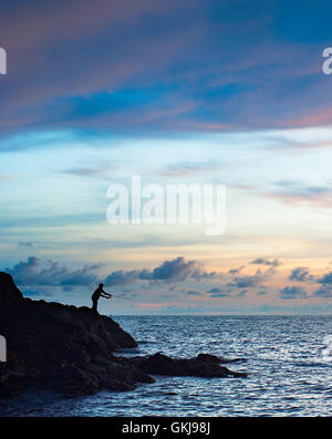 Silhouette di un pescatore al tramonto sulla riva del mare Foto Stock