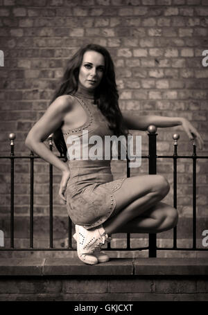 Atletico e muscolare di moda femminile modello sorge nella danza pongono contro un muro di mattoni che indossa in pelle scamosciata grigia outfit prigioniero, formatori di colore bianco Foto Stock