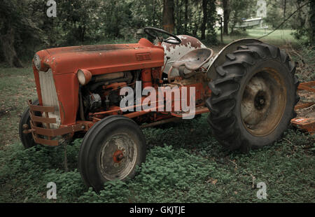 Un vecchio arrugginito orange il trattore in una zona boscosa. Foto Stock