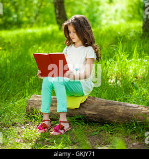 Affascinante piccolo ragazza nella foresta con libro sullo sfondo del parco di estate Foto Stock