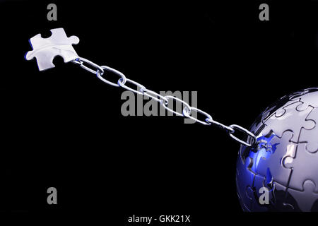 Pezzo del puzzle che cerca di fuggire dal mondo, legati da una catena su sfondo nero Foto Stock