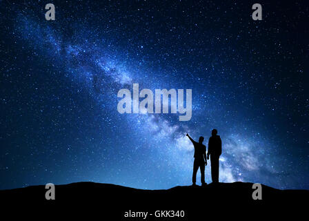 La Via Lattea con silhouette di uomini. Padre e figlio che puntare il dito nella notte cielo stellato sulla montagna. Paesaggio notturno. Foto Stock