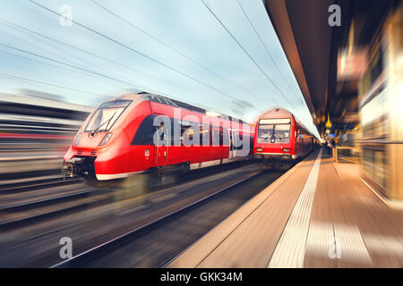 Moderna e alta velocità passeggeri rosso treni pendolari presso la stazione ferroviaria al tramonto. Stazione ferroviaria. Ferrovia Foto Stock