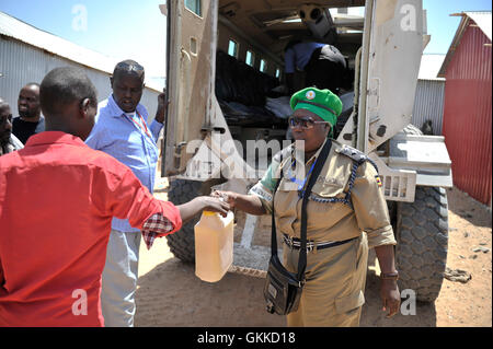 Officer Nakandha dell AMISOM la polizia di carichi un gallone di olio di cottura di Kaspi e mani di uno dei beneficiari di una dispensa alimentare a un IDP camp, Siliga Amerikanka, il 24 febbraio 2014 quando un gruppo di ufficiali di AMISOM alcune raccolte di denaro tra di loro e hanno comprato i prodotti alimentari per una comunità di 50 persone non vedenti. Foto Stock