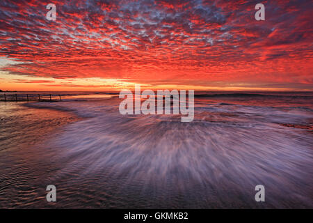 Sfocata onda veloce al golden ora oltre il piano fondale roccioso intorno al rock pool di Mona Vale Beach a Sydney. Foto Stock