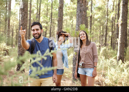 Un giovane uomo rivolto a qualcosa per i suoi amici in una foresta di pini nel tardo pomeriggio di sole, guardando avanti mentre indossa casu Foto Stock