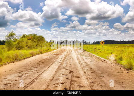 Girare a sinistra balck oltre il cartello giallo con suolo strada sabbiosa in campagna. Strada cinematografica verticale. Argentina. America del Sud Foto Stock