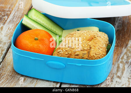 Una sana scatola di pranzo consistente misti formaggio grana rotolo, mandarino e bastoncini di cetriolo su una superficie di legno Foto Stock