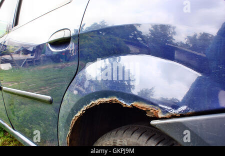 Notevolmente corroso rusty i passaruota in un auto blu Foto Stock