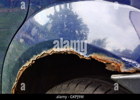 Notevolmente corroso rusty i passaruota in un auto blu Foto Stock