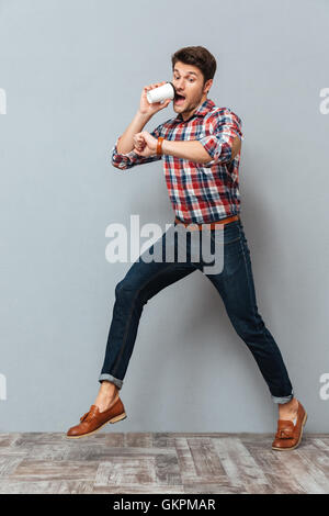 Scioccato giovane uomo a bere il caffè da asporto e in esecuzione su sfondo grigio Foto Stock