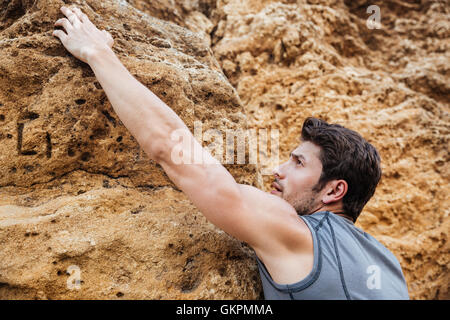 Uomo di raggiungere per un grip mentre lui rock si arrampica su di una ripida scogliera Foto Stock