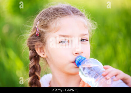 Poco carino ragazza sulla natura beve l'acqua da una bottiglia di plastica Foto Stock