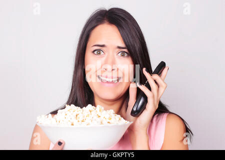 Giovane donna caucasica guardando un film / TV, mentre vi gustate uno snack. Ragazza mangiare popcorn con paura di espressione. Foto Stock