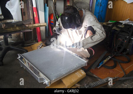 I thailandesi utilizzano l'elettricità di saldatura per fissare e saldare il radiatore di auto in garage locale a Nonthaburi, Tailandia Foto Stock
