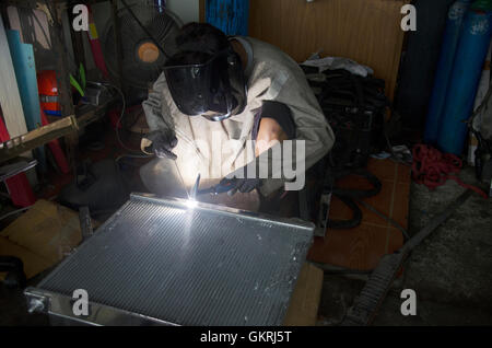 I thailandesi utilizzano l'elettricità di saldatura per fissare e saldare il radiatore di auto in garage locale a Nonthaburi, Tailandia Foto Stock