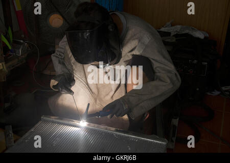 I thailandesi utilizzano l'elettricità di saldatura per fissare e saldare il radiatore di auto in garage locale a Nonthaburi, Tailandia Foto Stock