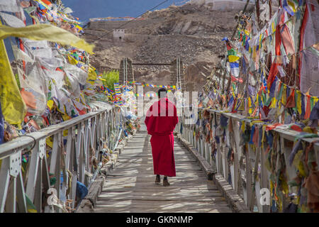 Un monaco passeggiate sul ponte sentiero circondato da colorati tibetano bandiere di preghiera , Ladakh , India Foto Stock