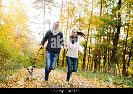 Bella coppia Giovane con cane che corre nella foresta di autunno Foto Stock