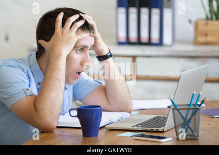 Giovane imprenditore ha sottolineato seduta con laptop e toccando con testa sconvolto l'espressione del viso. Sorpreso il business man cerca Foto Stock