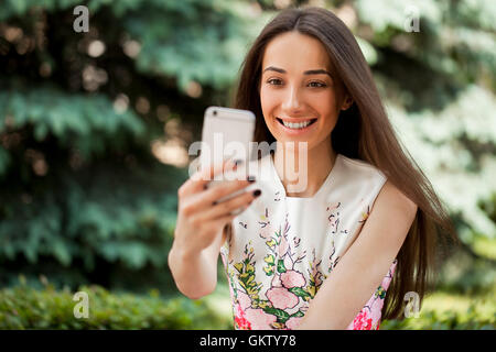 Bella e sorridente brunette donna prendere una immagine di se stessa con uno smartphone. selfie, estate all'aperto Foto Stock